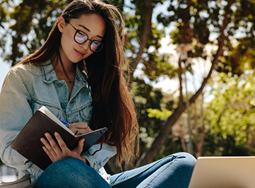 young adult female sitting outside writing in her notepad